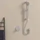 Duscharmatur von Ideal Standard mit Handbrause und Einsatz zur Temperaturregelung, montiert an einer hellen Wand, neben einem schwarzen Handtuchhalter.